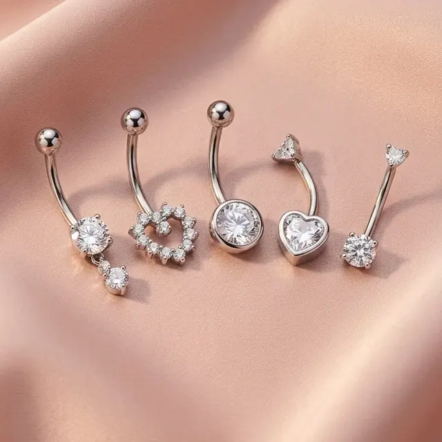 Conjunto de piercings prateados com coração e pedras sobre cetim rosé